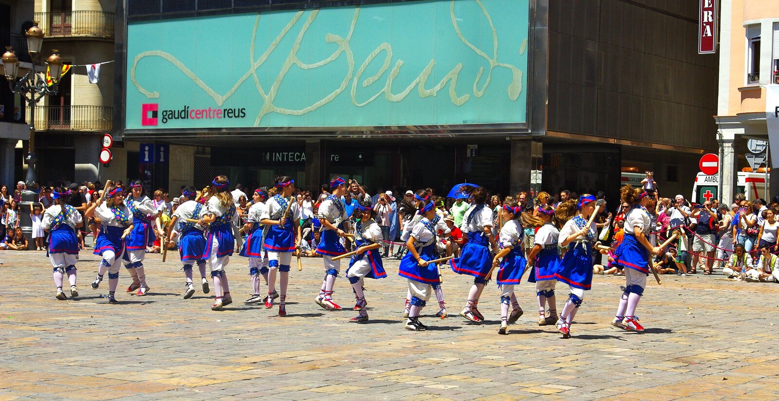A long formation of blue-and-white ball de bastons dancers crossing a sunny square during Reus Festa Major